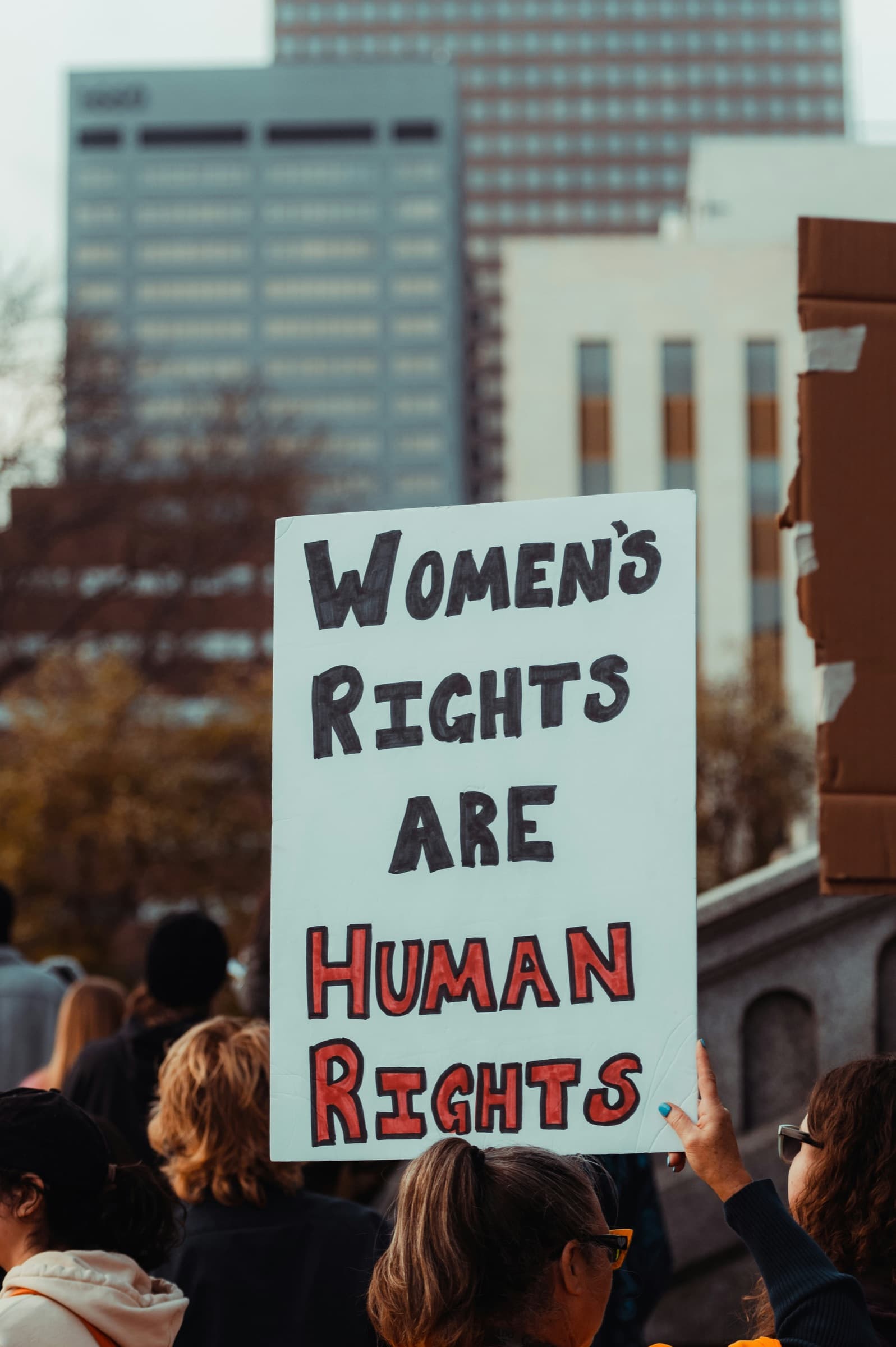 A woman in a city crowd holds up a sign that reads: Women's rights are human rights.
