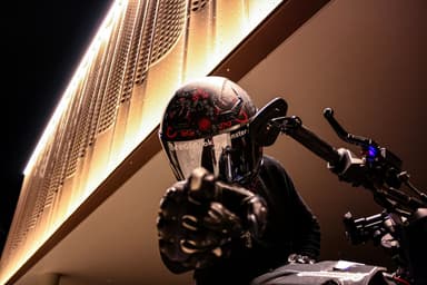 Cookie on a motorbike at night in a full-face helmet, pointing at the camera.