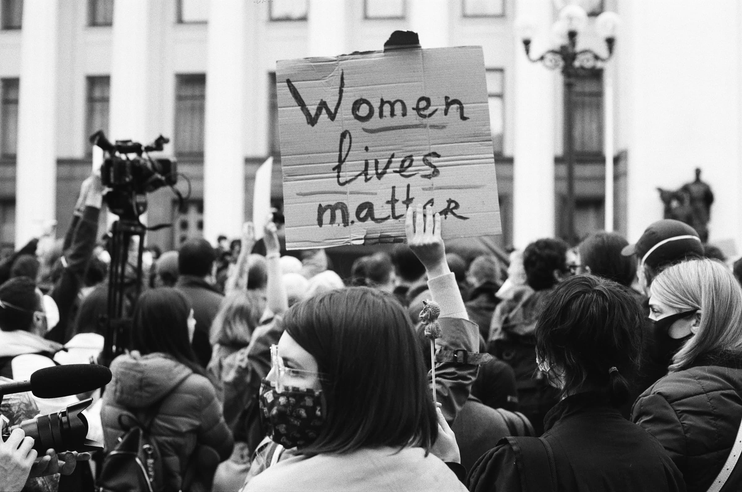 A woman in a crowd holds up a cardboard sign that reads: Women lives matter.